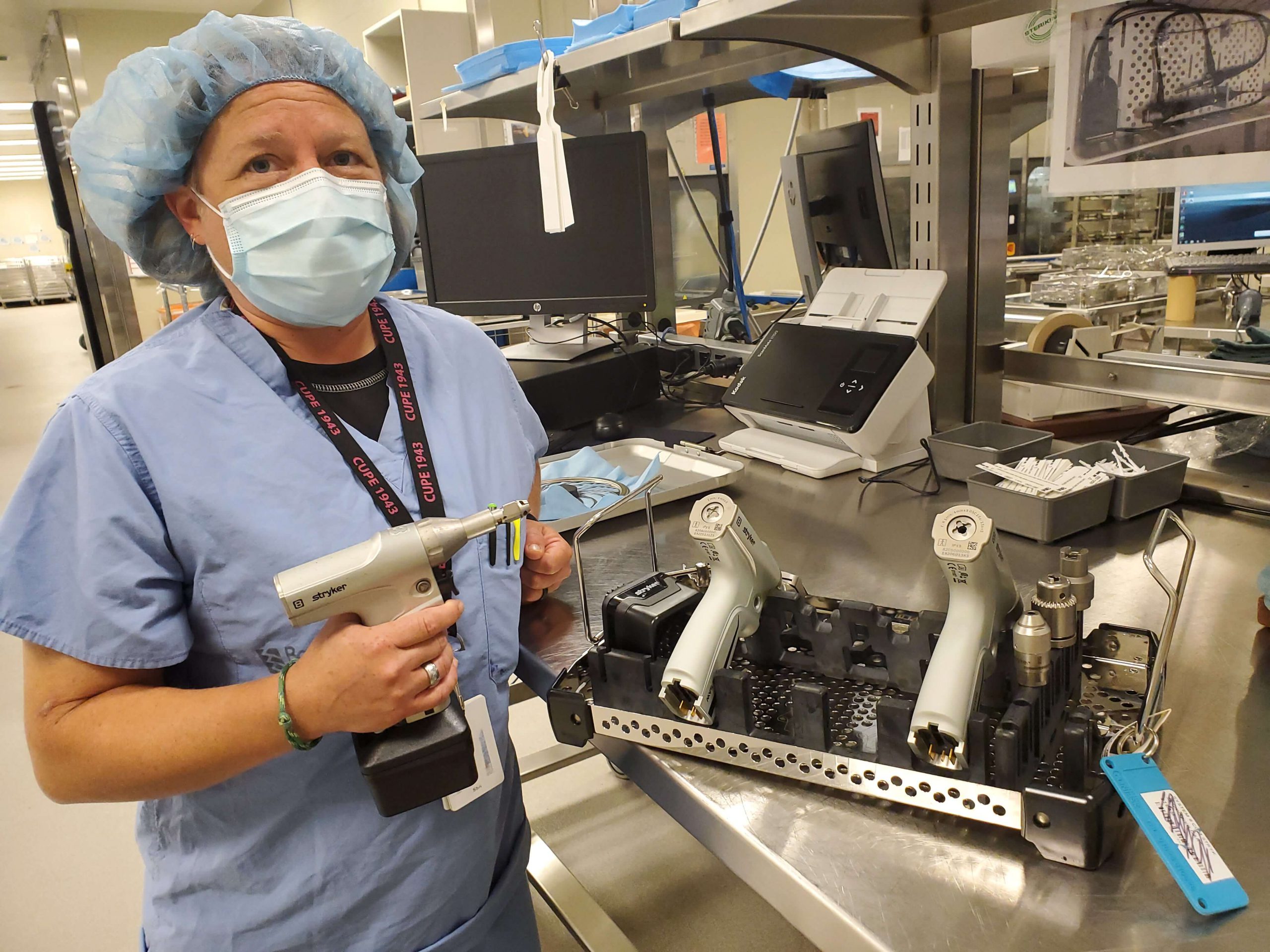 Masked surgical suite assistant holds a surgical tool